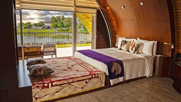 A bedroom with a large bed, a view of a lake, and a wooden ceiling. - NIRVANA RETREAT (Ras Al Khaimah)