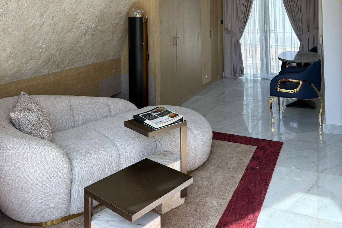 A modern living room with a high ceiling, a built-in staircase, a sectional sofa, a coffee table, and a view of the outdoors.