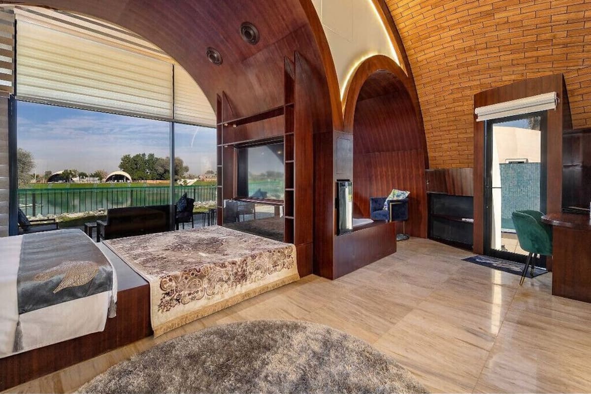 A spacious room with a large bed, a desk, and a view of a green landscape.