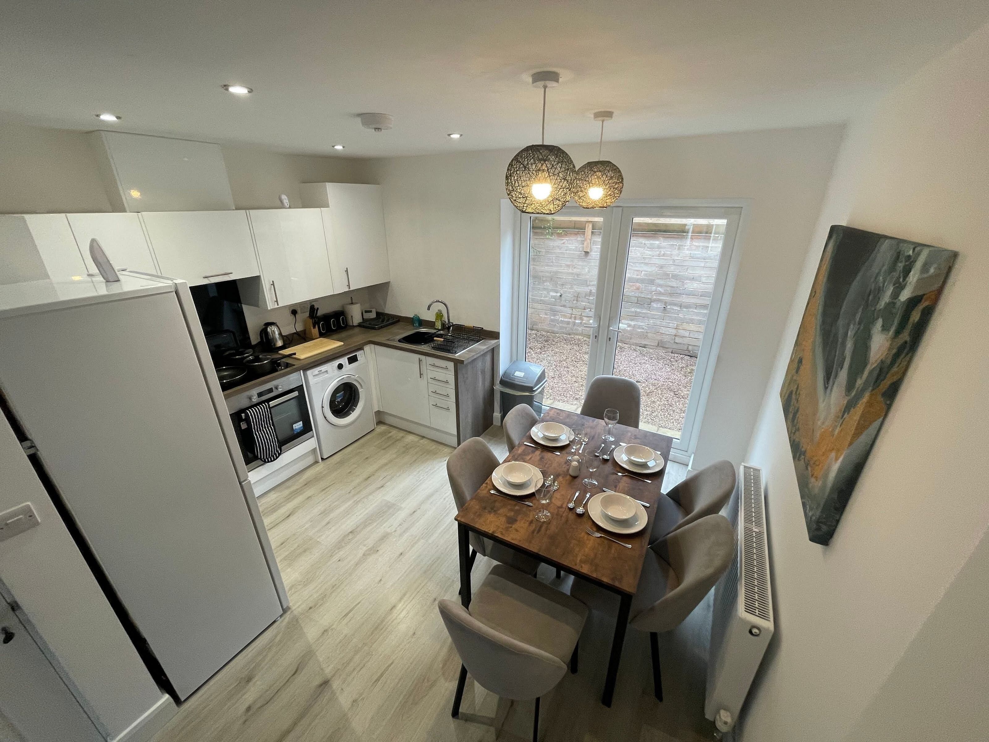A modern kitchen with a dining area, including a table set for four, a washing machine, and a refrigerator.