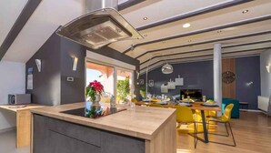 Una cocina moderna con una isla central, un comedor con sillas amarillas y un ventanal grande.