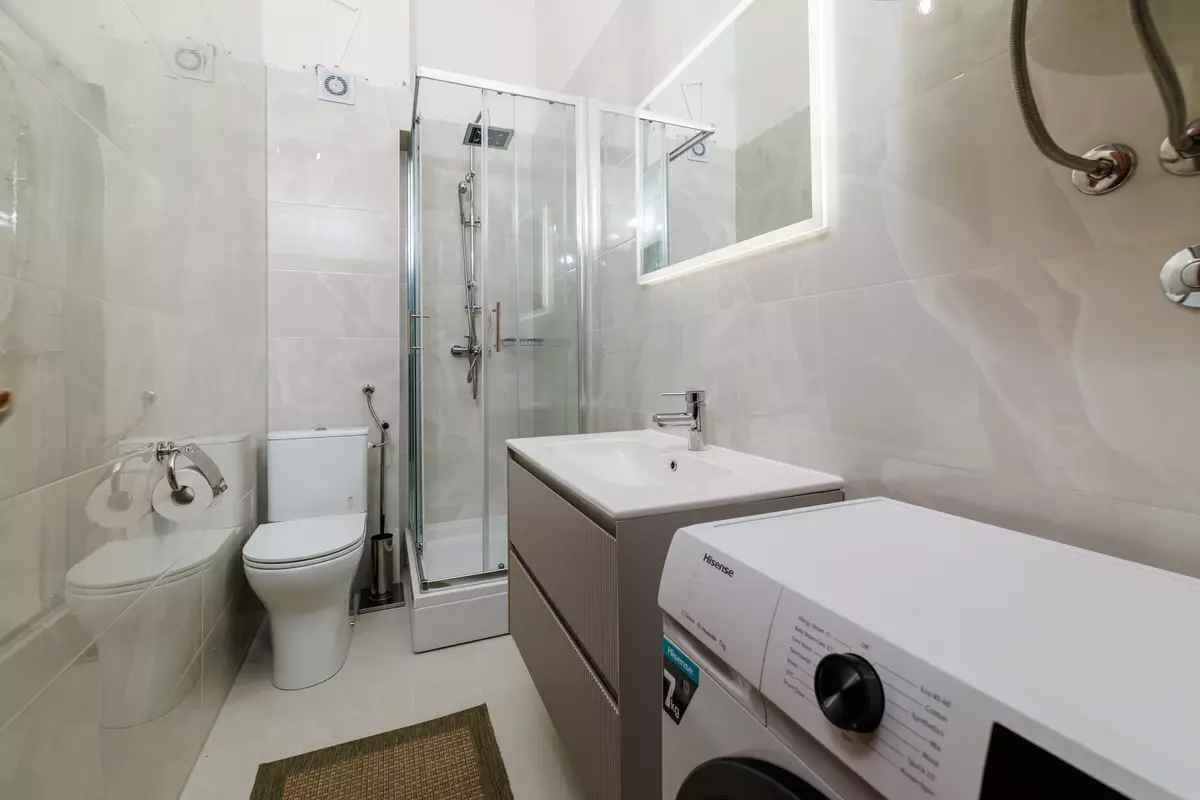 A bathroom with a glass shower enclosure, a toilet, a sink, and a washing machine.