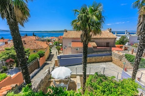 Ein Küstenwohngebiet mit Häusern mit Terrakotta-Dächern, Palmen und freiem Blick auf das Meer.
