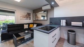 Een moderne keuken met een centraal kookeiland, een zwarte bank met kussens, een koffieapparaat en een prullenbak.