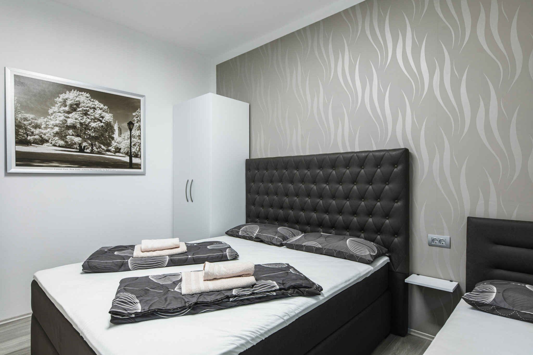 Un dormitorio moderno con cabecera capitonada, una cama grande con ropa de cama estampada, un armario y un cuadro en la pared.