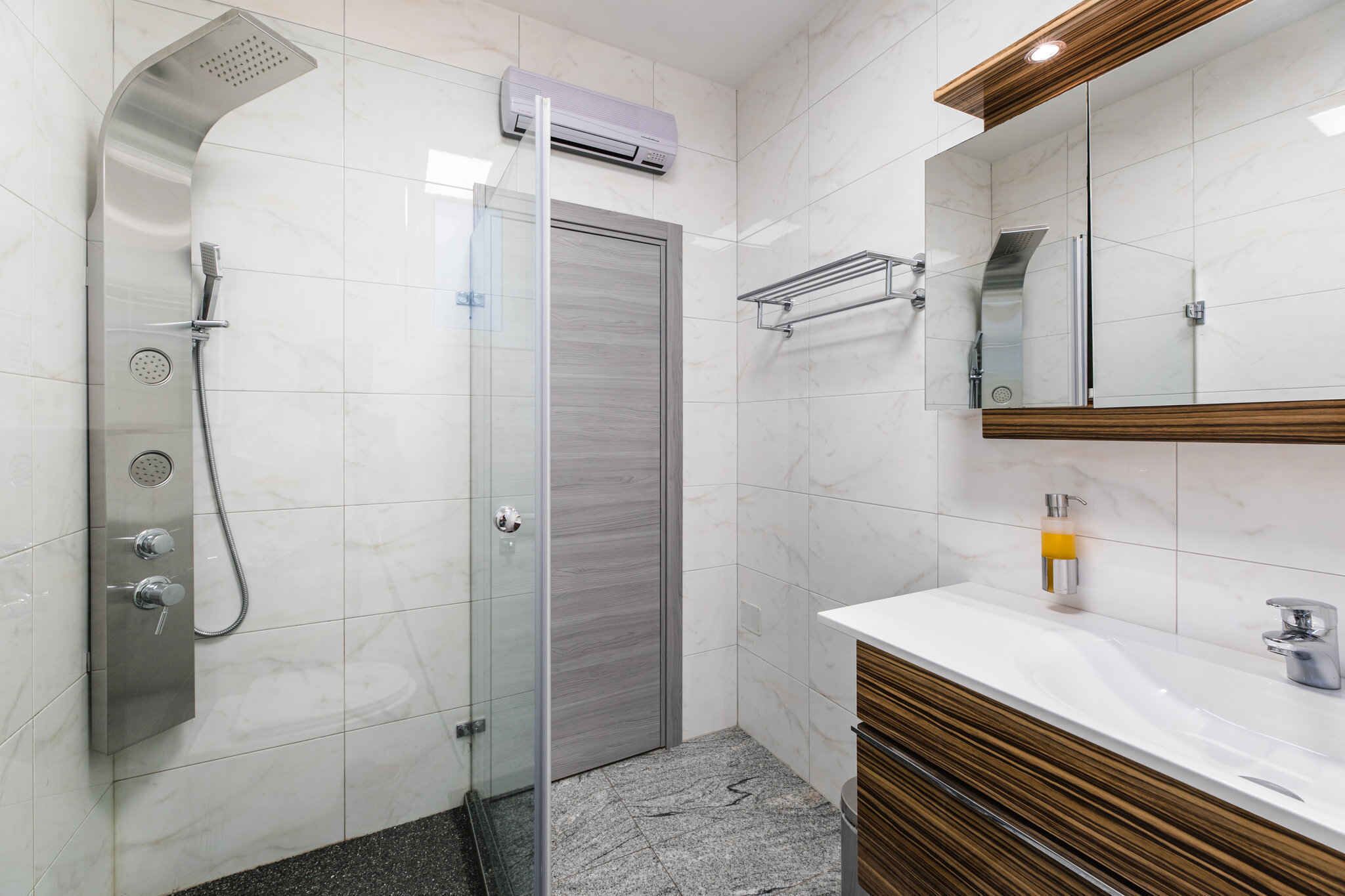 Ein modernes Badezimmer mit einer gläsernen Dusche, einem weißen Marmorwaschbecken und einem hölzernen Waschtisch.
