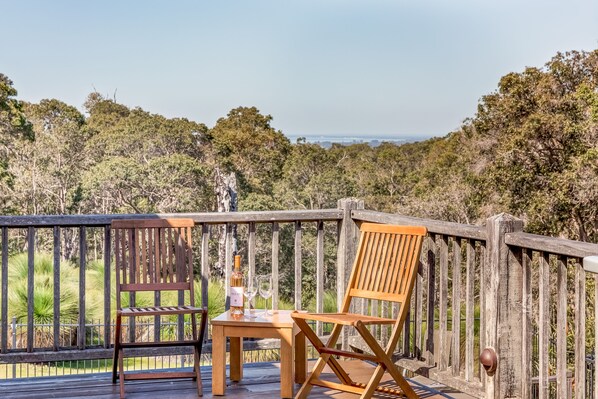 Terraza de madera con una mesa y dos sillas, con vistas a un área boscosa.