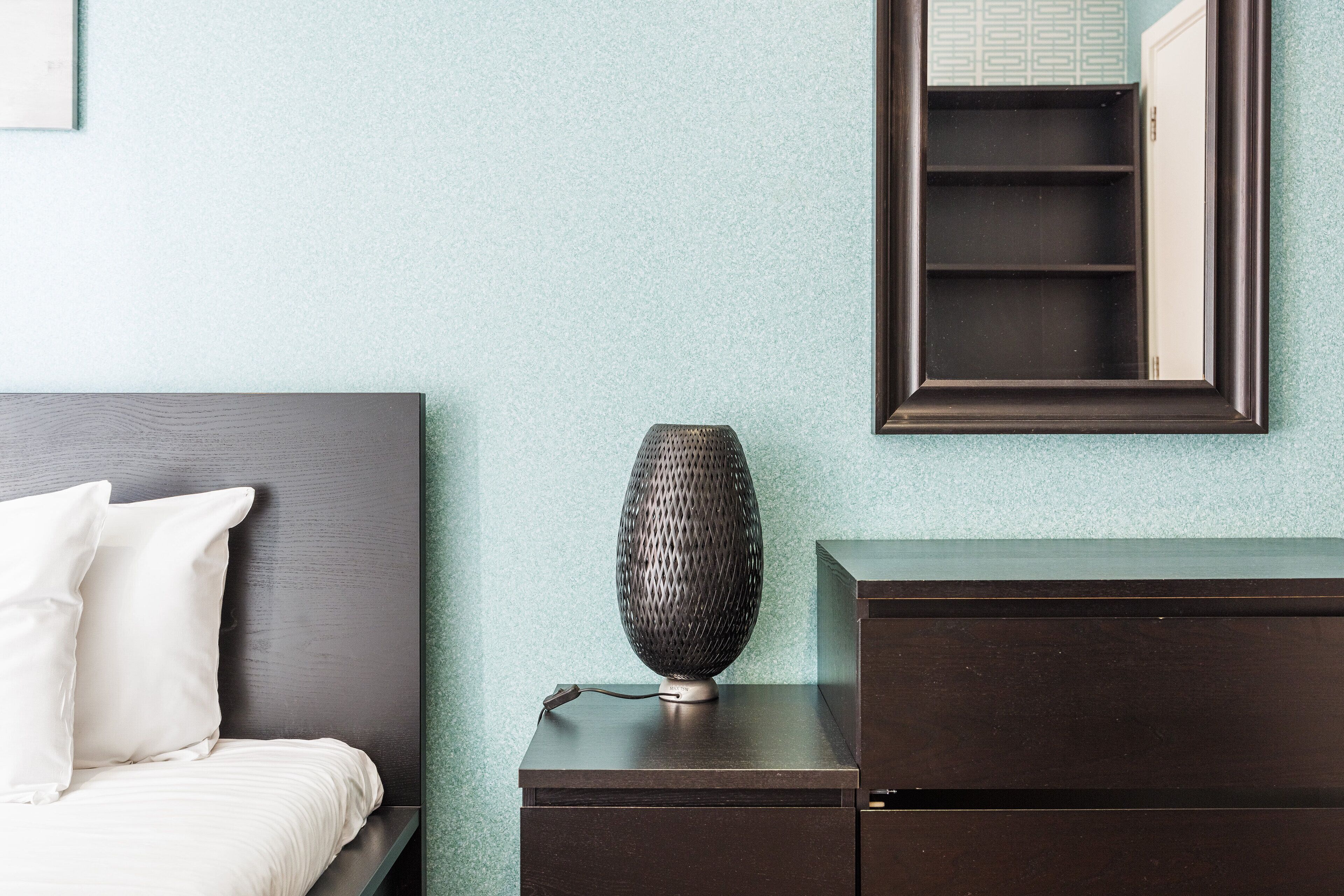 Une chambre à coucher bien rangée, avec un lit, une table de chevet dotée d’une lampe et une commode.
