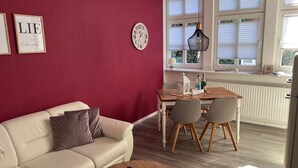 Una sala de estar acogedora con una pared roja, un sofá blanco y un comedor con una mesa y sillas de madera.