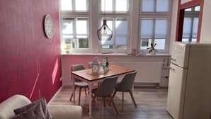 Una cocina compacta con una mesa de comedor, sillas, un refrigerador y una ventana con persianas.