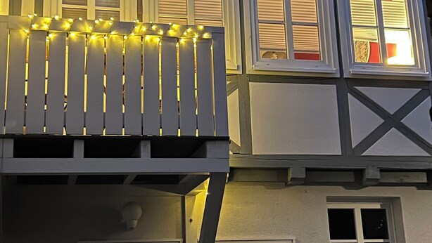 Un edificio de varios pisos con un balcón decorado con luces de cadena, múltiples ventanas con contraventanas y una antena parabólica visible.