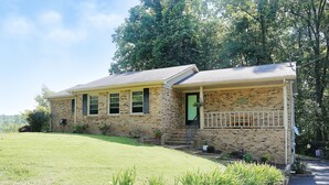 A brick house with a front porch, a green door, and a small front yard. - Cozy Country Cottage (Culleoka)