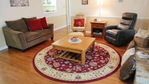 A living room with a brown sofa, a wooden coffee table, a red and beige patterned rug, a leather armchair, and a small side table with a lamp. - Cozy Country Cottage (Culleoka)