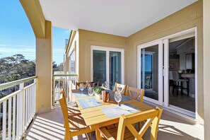 A balcony with a wooden table set for dining, featuring a glass of wine and a plant. - Top Floor Oceanfront 3 Bedroom villa with panoramic views and community pool (Hilton Head Island)