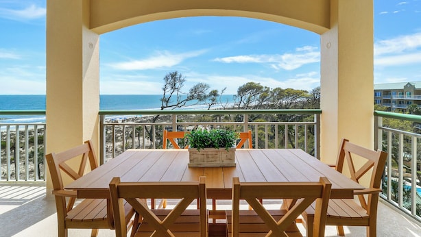 Une table et des chaises en bois sur un balcon offrant une vue sur la plage et l’océan.