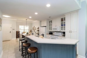 A kitchen with white cabinets, a blue island, and bar stools.