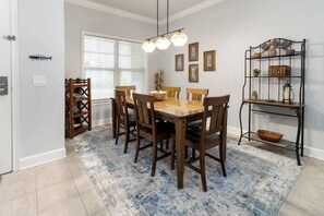 A dining area with a wooden table and chairs, a patterned rug, and wall-mounted shelves with decorative items.