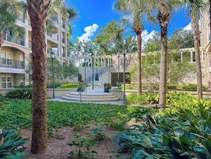 A courtyard with palm trees, a covered staircase, and a building with balconies.