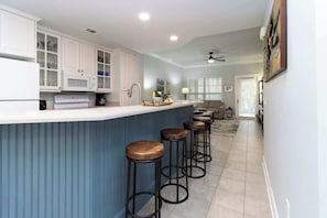 A kitchen with white cabinets, a central island with stools, and a dining area with a sofa.