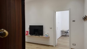 Une pièce avec un téléviseur posé sur un meuble en bois, une petite table avec une chaise, et une porte donnant sur une autre pièce.