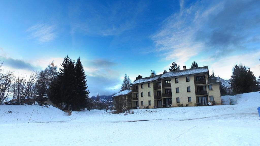 A multi-story building with a snow-covered roof, surrounded by trees and a clear sky.