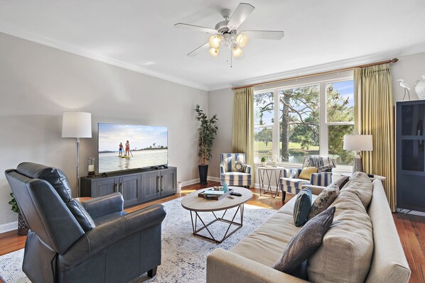 A living room with a sofa, armchair, coffee table, TV, and a large window with curtains. - Lake & Golf Course View ~ 6 Seat Golf Cart (Miramar Beach)
