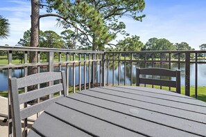 A wooden deck with a metal railing overlooking a calm lake, surrounded by trees. - Lake & Golf Course View ~ 6 Seat Golf Cart (Miramar Beach)