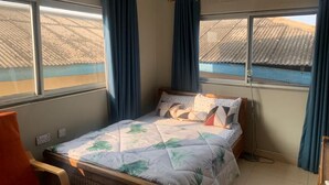 A single bed with a floral bedspread, a wooden headboard, and a window with curtains. - 2 Bedroom Cozy Apartment. (Accra)