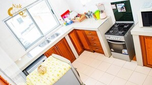 A compact kitchen with a stove, oven, sink, and a window. - 2 Bedroom Cozy Apartment. (Accra)