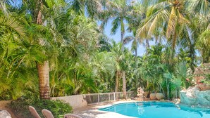 Zona junto a la piscina con sillones de descanso y una vista despejada de una alberca rodeada de exuberante vegetación.