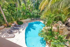 A swimming pool surrounded by lush greenery, with lounge chairs and a stone wall.