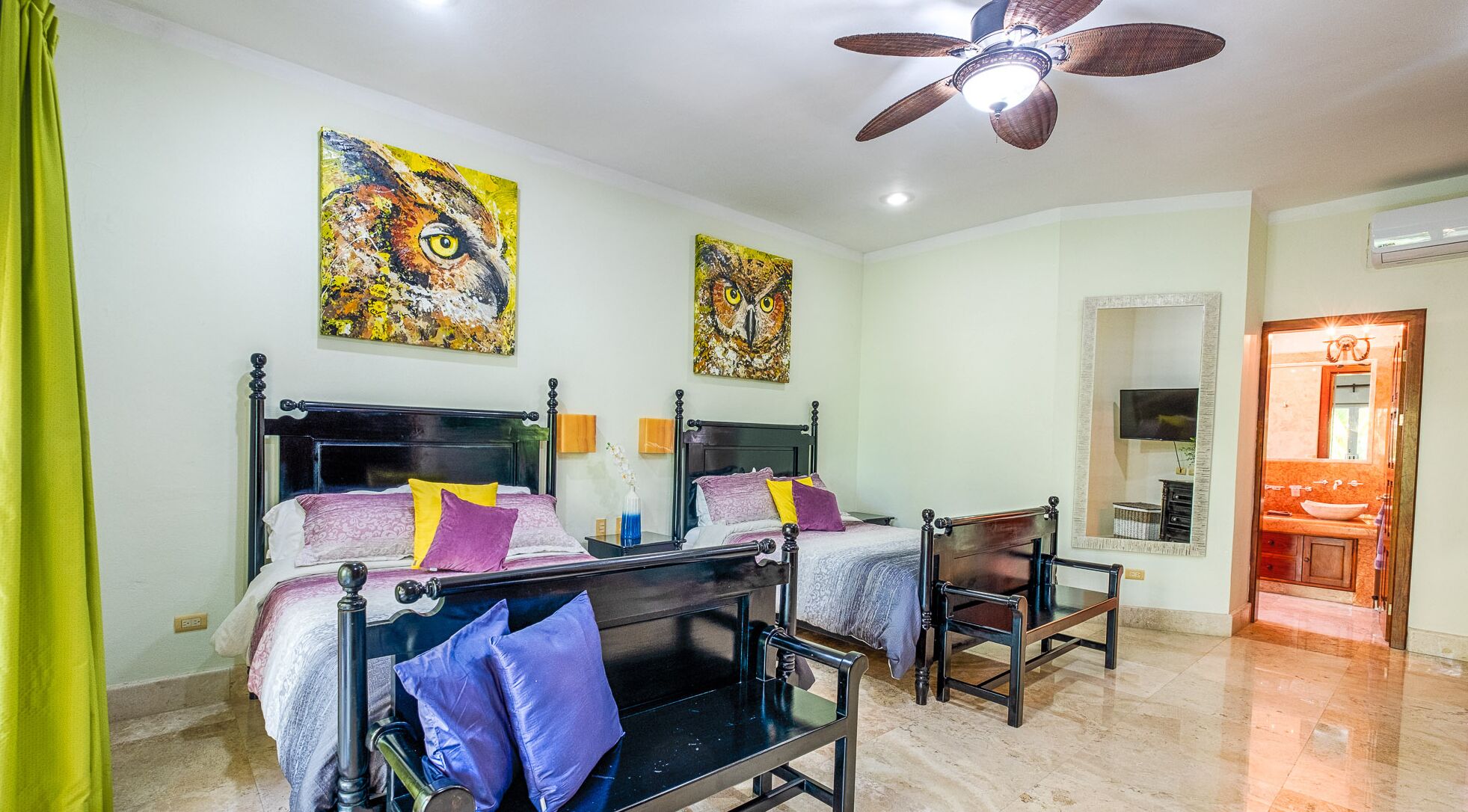 A hotel room with two beds, a chair, a ceiling fan, and artwork on the walls.