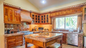 Una cocina con armarios de madera, encimeras de granito, una isla central, una estufa, un microondas y un lavavajillas.