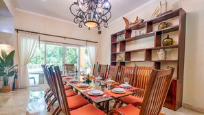 A dining area with a glass table, wooden chairs, and a bookshelf with decorative items.