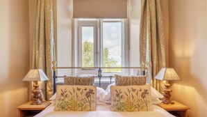 Una cama bien hecha con almohadas estampadas, una ventana con cortinas y dos lámparas de noche.