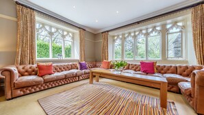 Un salón amplio con un sofá grande de cuero marrón, una mesa de centro de madera y una alfombra con rayas de colores.