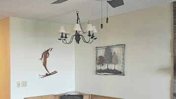 En spiseplads med en træbænk og et bord, en ventilator i loftet, en lysekrone og billedkunst på væggene.