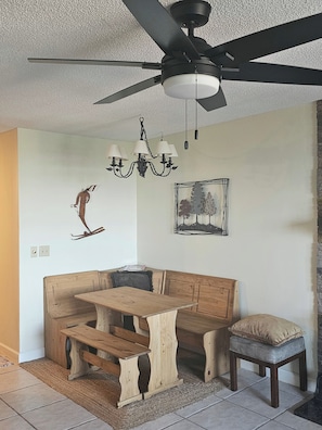 A dining area with a wooden bench and table, a ceiling fan, a chandelier, and wall art.