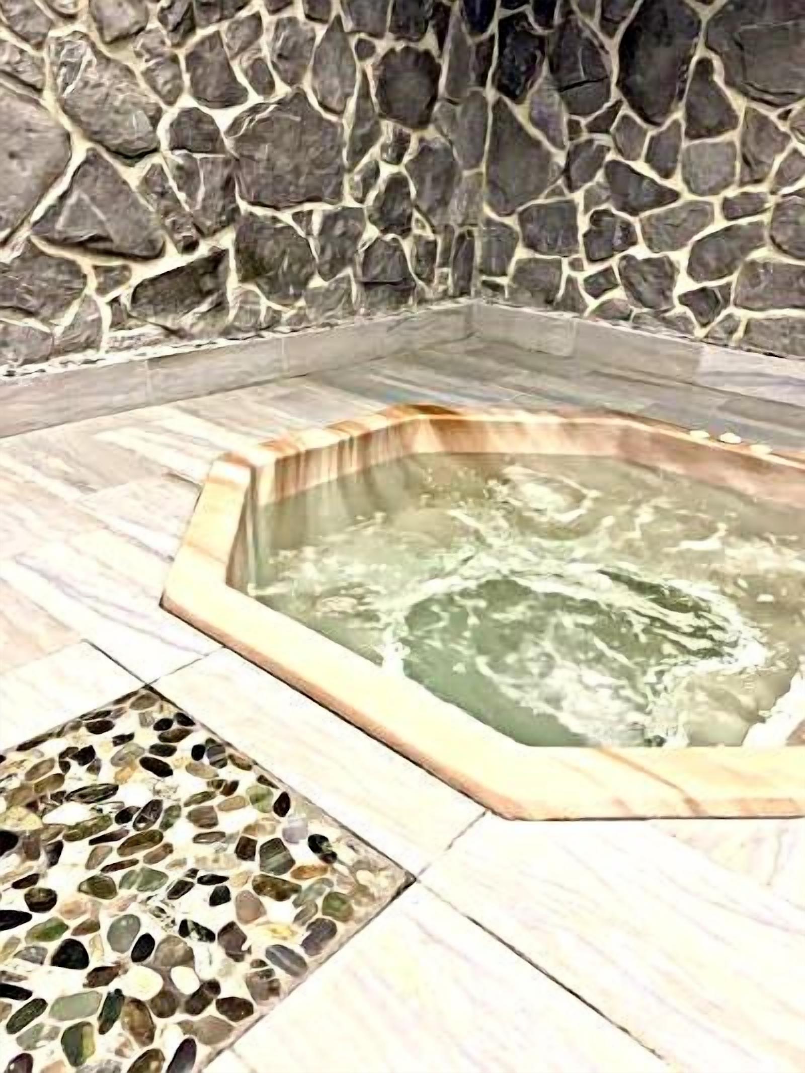A stone wall surrounding a hot tub area with a mosaic tile floor.