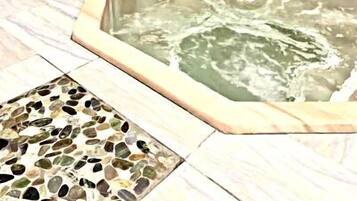 A stone wall surrounding a hot tub area with a mosaic tile floor.