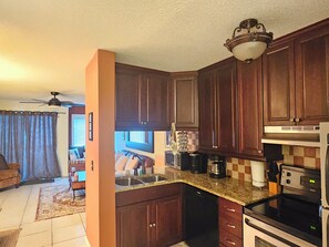 A kitchen with dark wooden cabinets, a granite countertop, a dishwasher, a stove, and a ceiling fan.