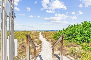 A sandy path leading to a beach with umbrellas and greenery.