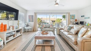 Ein geräumiges Wohnzimmer mit großem Fenster, Deckenventilator und einem beigefarbenen Sofa.