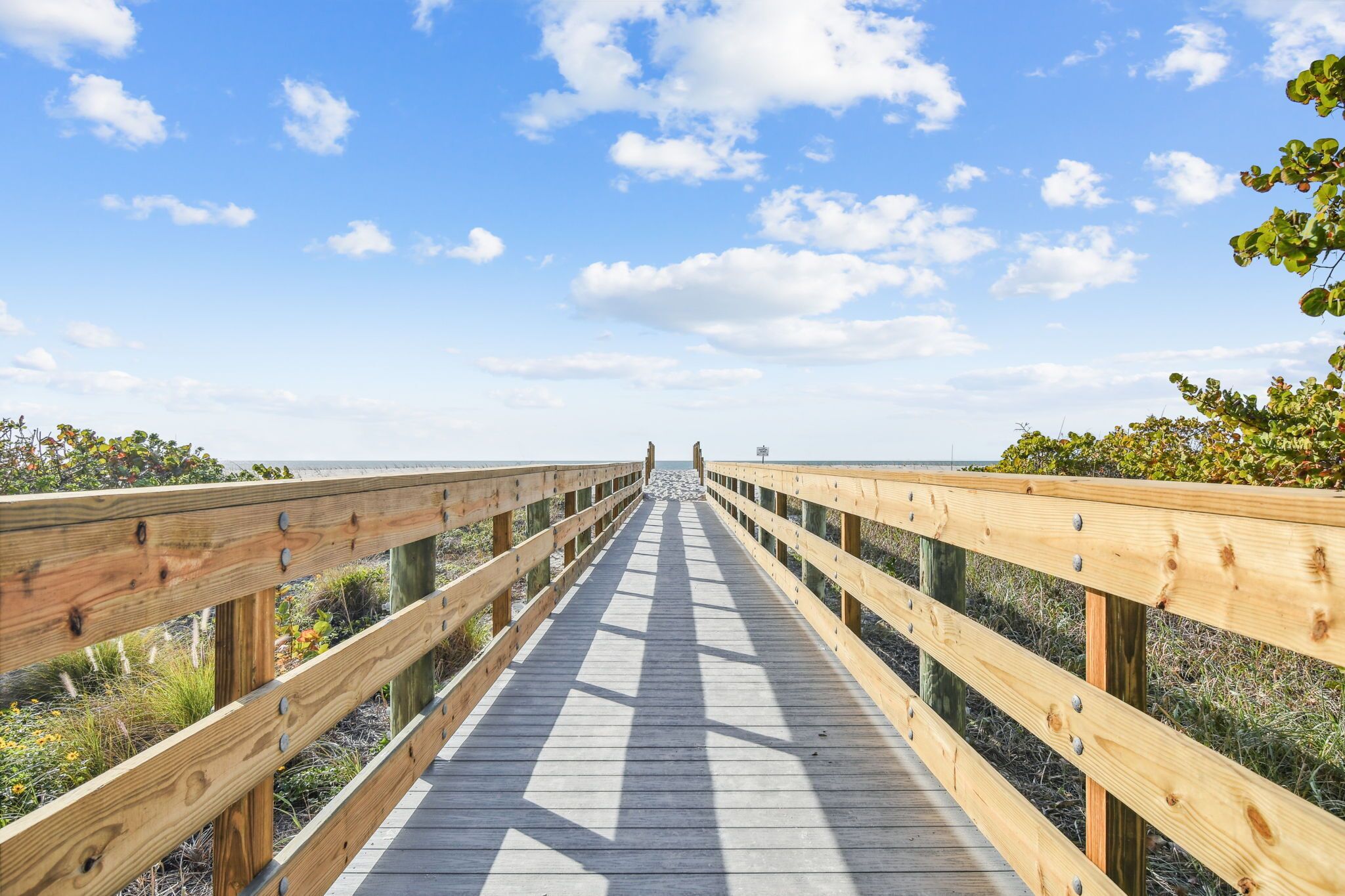 Une promenade en bois qui mène à une plage, avec un ciel dégagé.