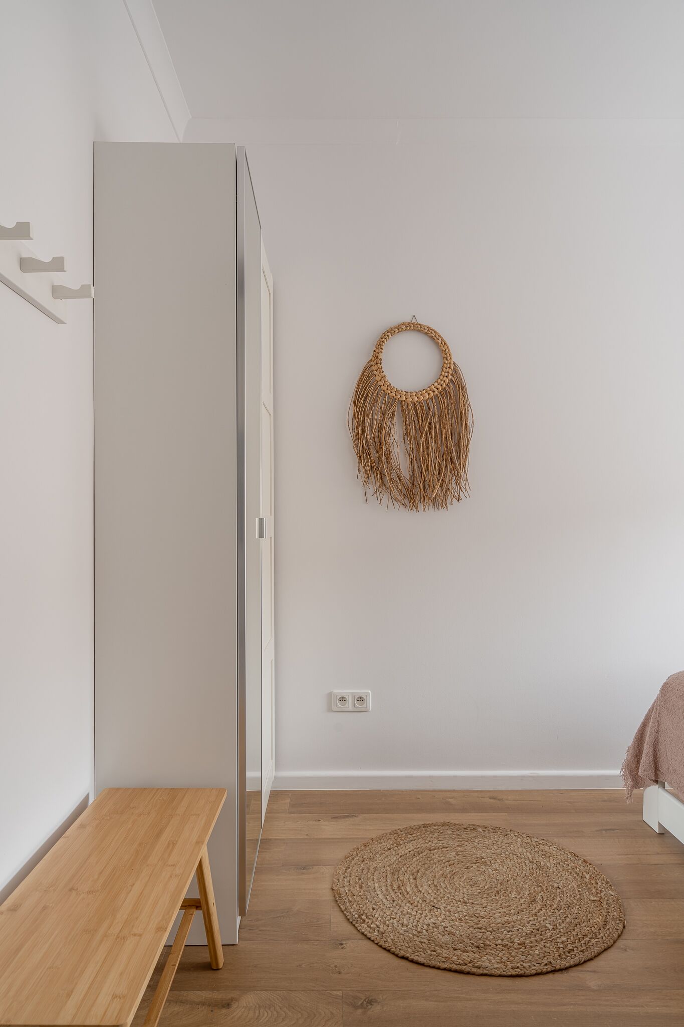 A minimalist room with a wooden bench, a woven rug, and a wall-mounted macrame piece.