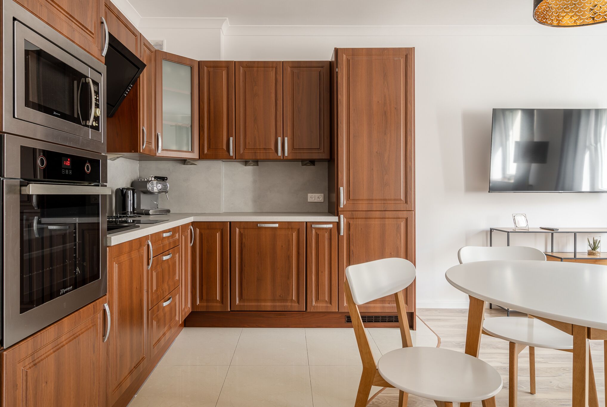 Una cucina moderna con mobili in legno, elettrodomestici in acciaio inossidabile e un'area pranzo con tavolo e sedie bianche.