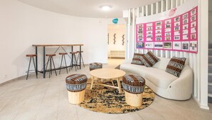Ein modernes Wohnzimmer mit einer Couch, einem runden Couchtisch und Barhocker. An der Wand hängt ein Korkbrett mit Fotos.