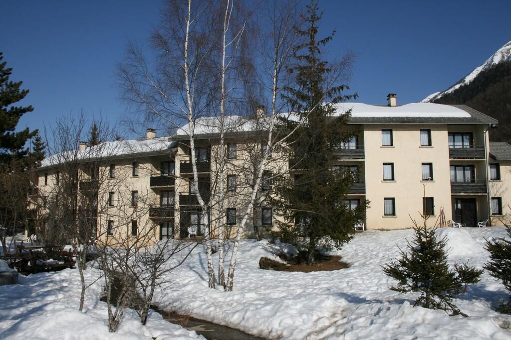 Un edificio de varios pisos con tejado nevado, rodeado de árboles y un paisaje montañoso.