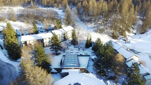 An aerial view of a resort with multiple buildings, a swimming pool, and surrounding snow-covered landscape.