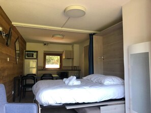 A compact room with a bed, a small kitchenette, and a seating area.